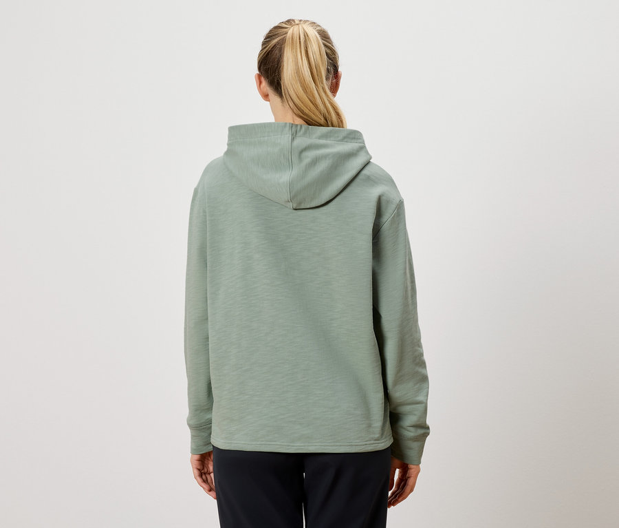 Vue arrière d'une femme avec une queue de cheval blonde portant un sweat à capuche vert clair et un pantalon noir.