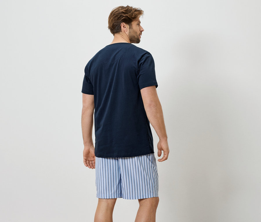 Homme vu de dos portant un t-shirt bleu marine et un boxer rayé sur un fond blanc.