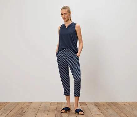 Femme debout, mains dans les poches, portant un haut bleu marine, un pantalon à motifs et des sandales bleues.