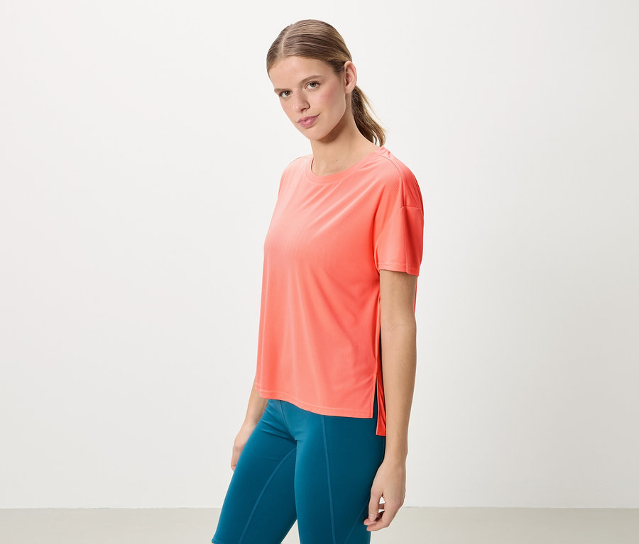 Femme avec queue de cheval portant un t-shirt corail et un legging bleu.