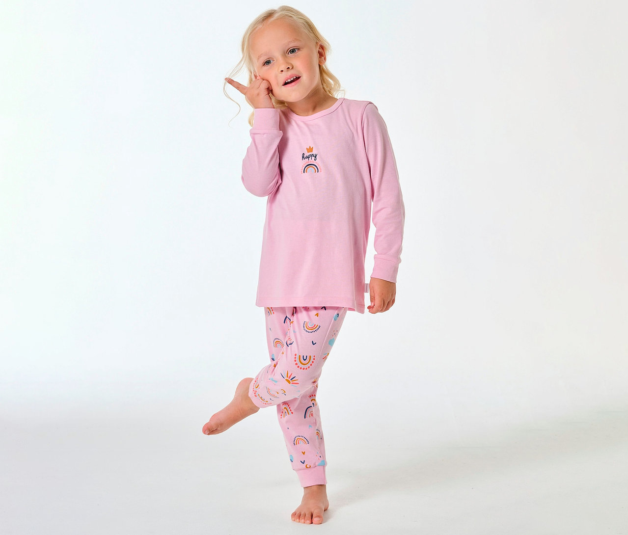 Fillette portant un pyjama long pour enfant SCHIESSER avec motif arc-en-ciel sur le pantalon et le haut.