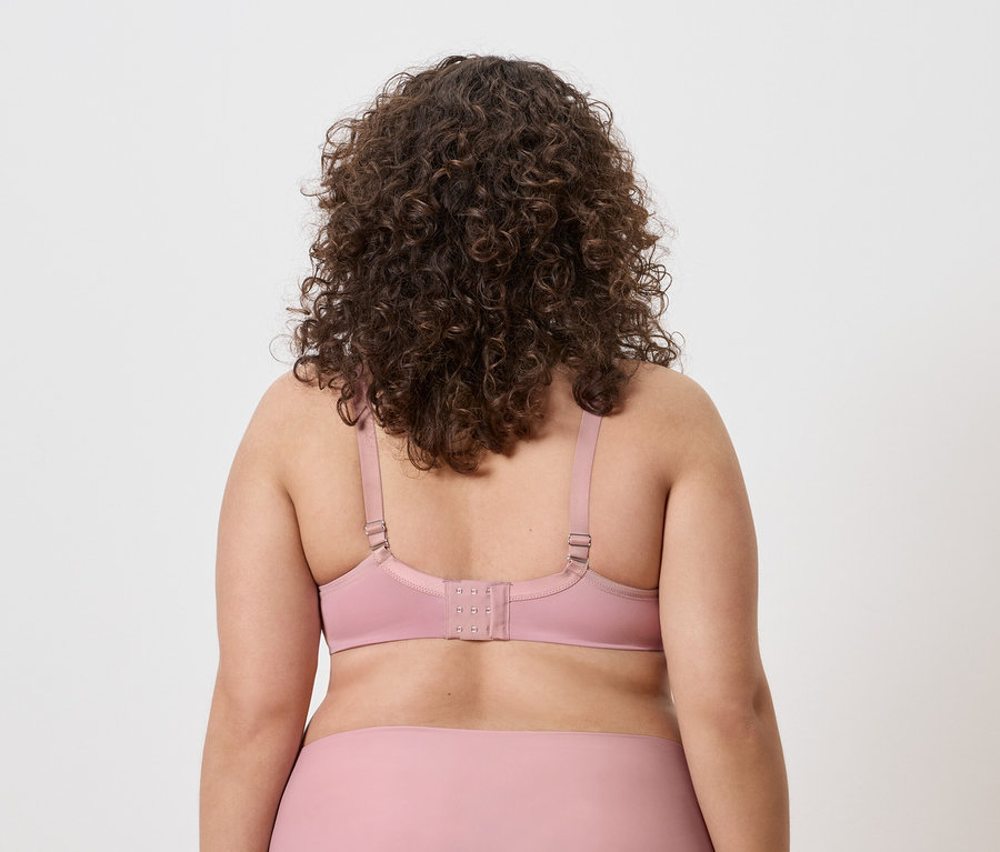 Vue arrière d'une femme aux cheveux bouclés portant un soutien-gorge rose.
