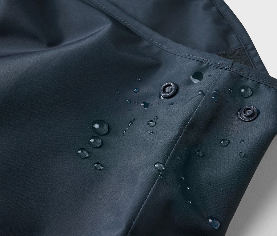 Gros plan de gouttes d'eau sur un tissu bleu marine avec deux boutons-pression.