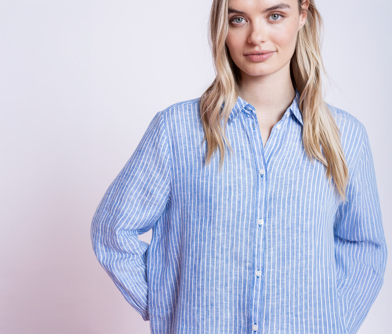 Une femme blonde portant une chemise rayée bleu et blanc regarde l'objectif.
