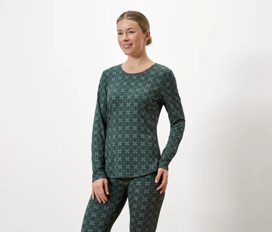 Femme portant un haut à manches longues et un legging vert foncé à motifs sur fond blanc.