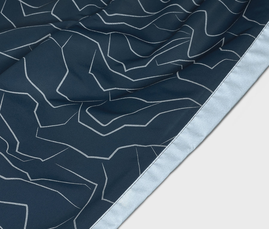 Gros plan d'un tissu bleu marine avec un motif de lignes blanches abstraites et une bordure argentée.