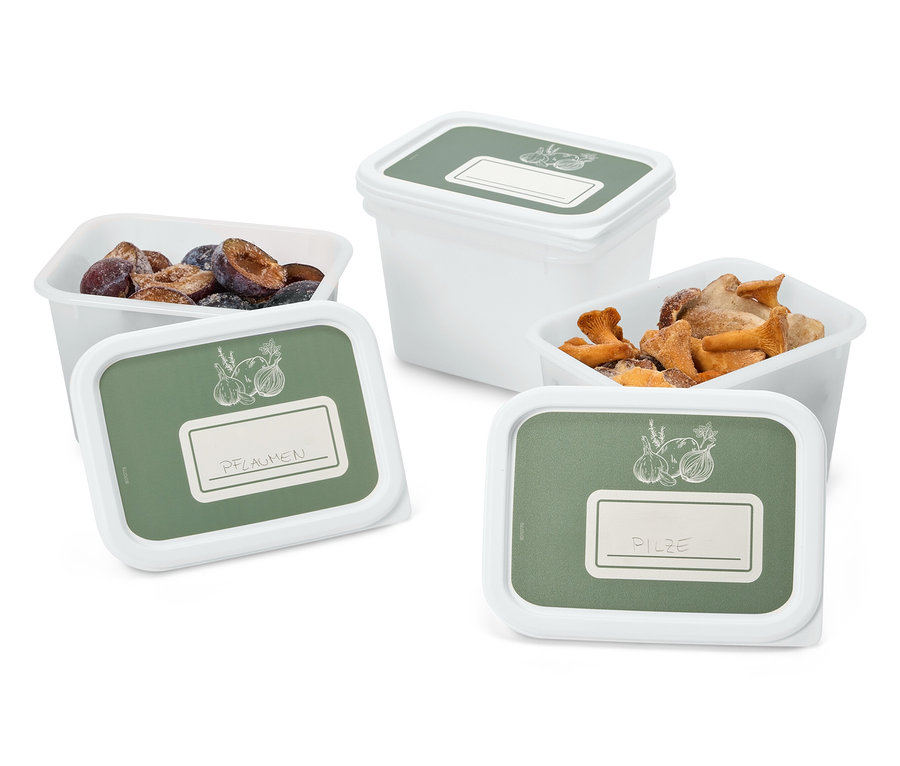 Quatre récipients blancs avec des couvercles verts, étiquetés « Prunes » et « Champignons », remplis de prunes et de champignons.
