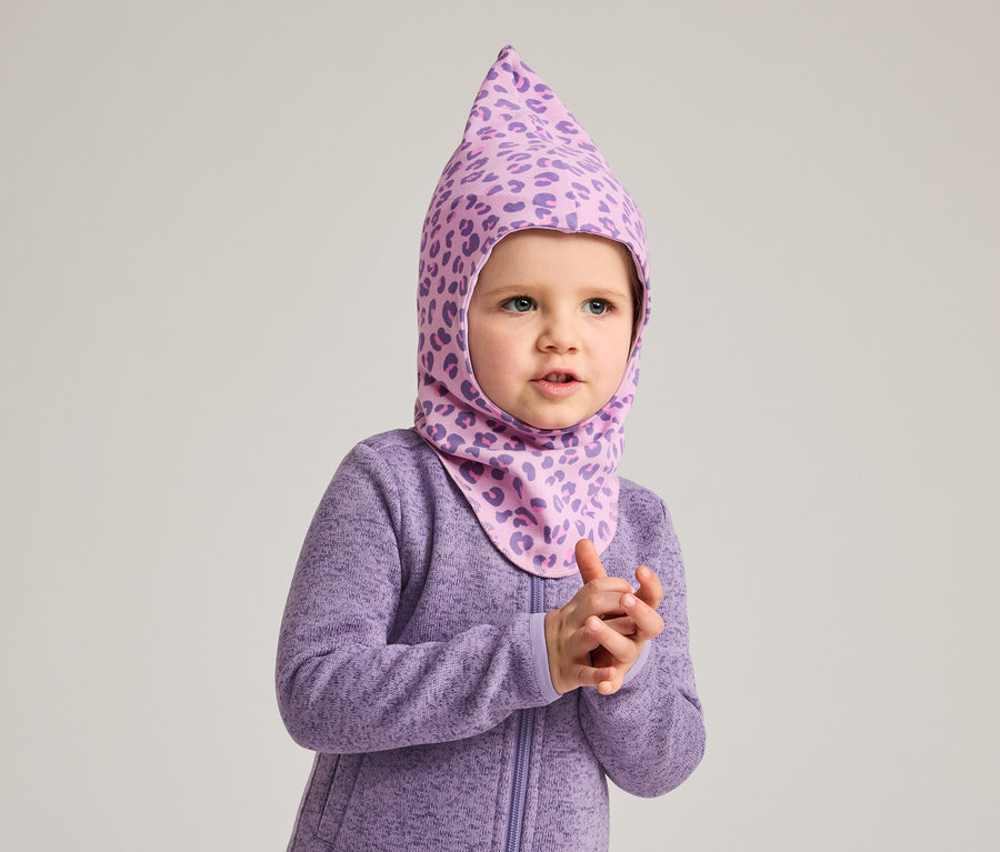 Un jeune enfant porte une combinaison violette et une cagoule violette à motif léopard.