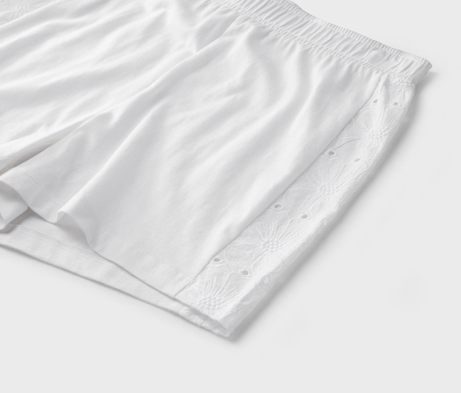 Gros plan d'un short blanc avec une taille élastique et des détails de broderie anglaise sur le côté.