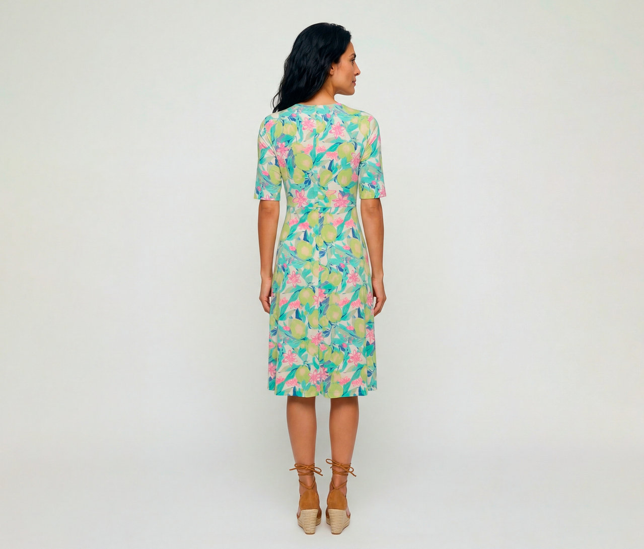 Femme vue de dos portant une robe en jersey Olsen avec un motif coloré de citrons verts et de fleurs roses, associée à des sandales compensées espadrilles marron.