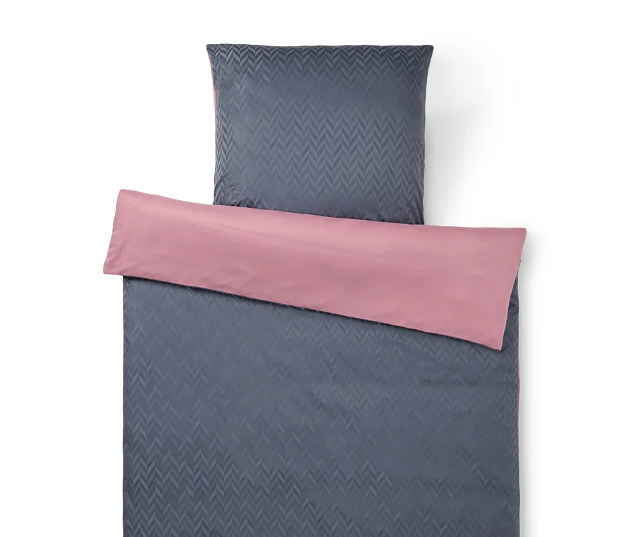 Parure de lit anthracite à motif chevrons, avec une taie d'oreiller et une housse de couette pliée pour révéler son côté rose.