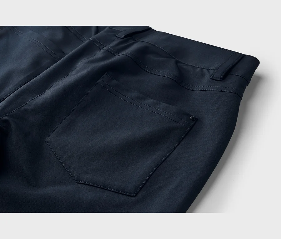 Gros plan du dos d'un pantalon bleu foncé, montrant une poche arrière plaquée avec des coutures visibles, un petit détail circulaire et la ceinture avec des passants.