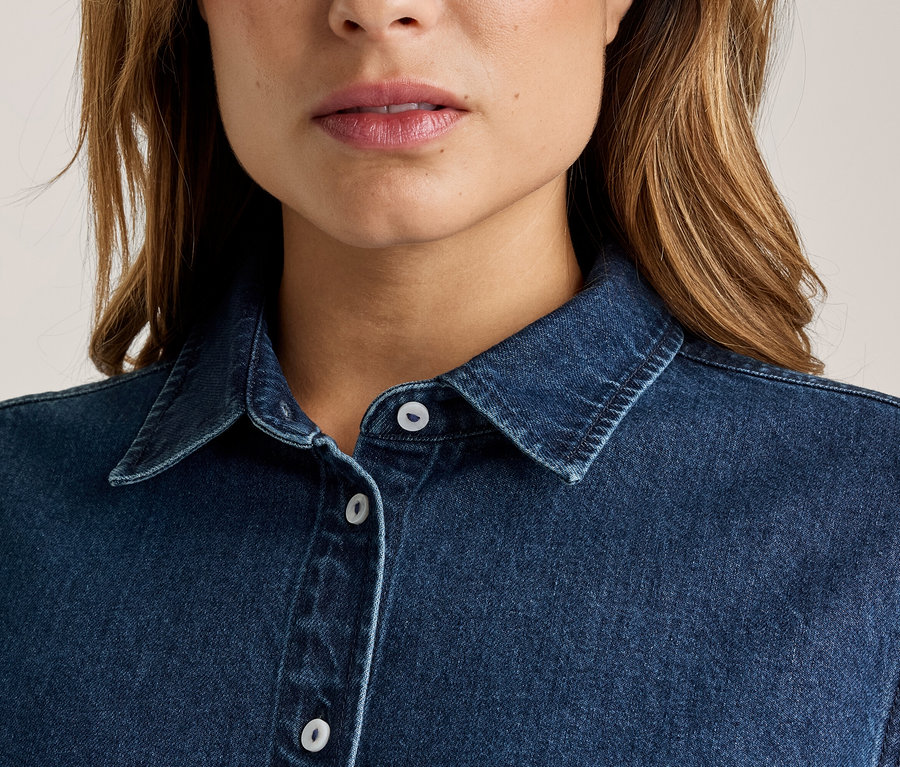 Gros plan d'une femme portant une chemise en jean bleu foncé avec un col et des boutons blancs, la bouche légèrement ouverte.