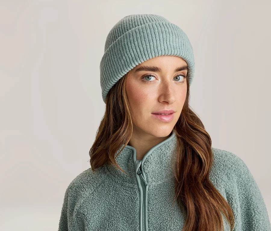 Gros plan d'une femme aux longs cheveux bruns portant un bonnet côtelé bleu clair et une veste polaire zippée bleu clair, regardant directement le spectateur.