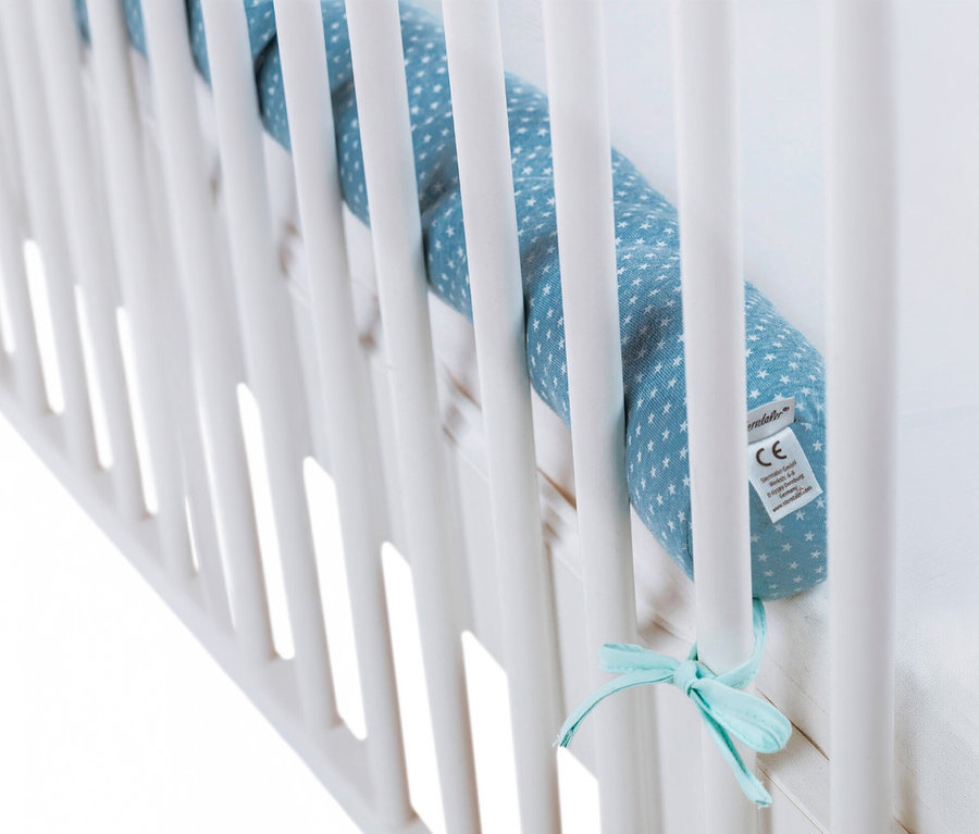 Un tour de lit bleu à étoiles blanches est attaché aux barreaux blancs d'un lit bébé avec un nœud bleu clair.