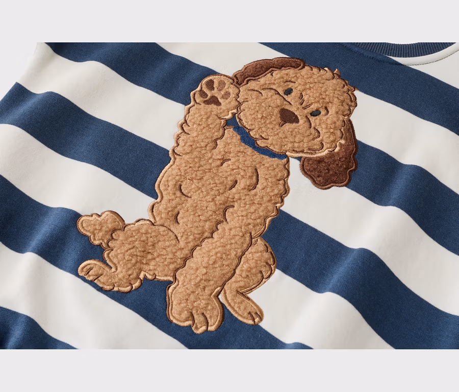Gros plan d'un vêtement rayé blanc et bleu marine avec une application de chien marron et moelleux portant un collier bleu, une patte levée.