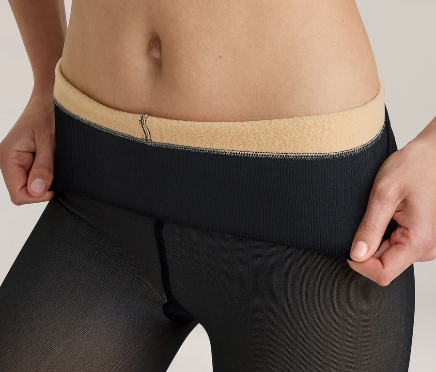 Torse d'une personne montrant les mains tirant la ceinture côtelée noire d'un collant noir transparent pour révéler une doublure intérieure beige et polaire.