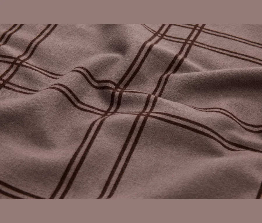 Gros plan d'un tissu drapé brun clair avec un motif à carreaux brun foncé, montrant des plis doux et la texture.