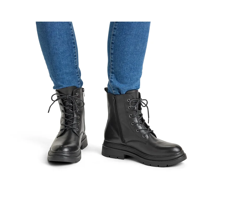 Jambes d'une personne portant un jean bleu et des bottines lacées noires à semelles épaisses.