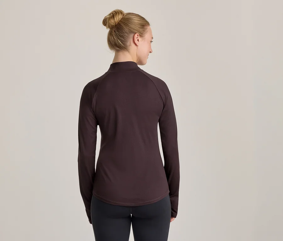 Femme de dos portant un haut à manches longues marron foncé et un legging noir, regardant légèrement sur le côté.