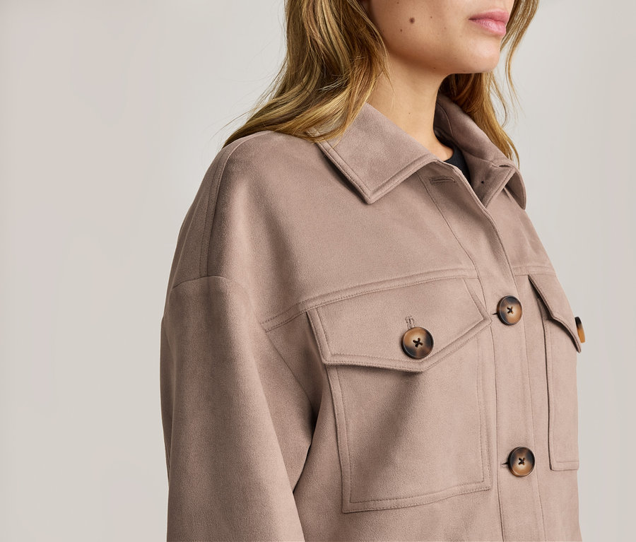 Femme portant une veste beige clair à col avec de grands boutons marron et deux poches poitrine.