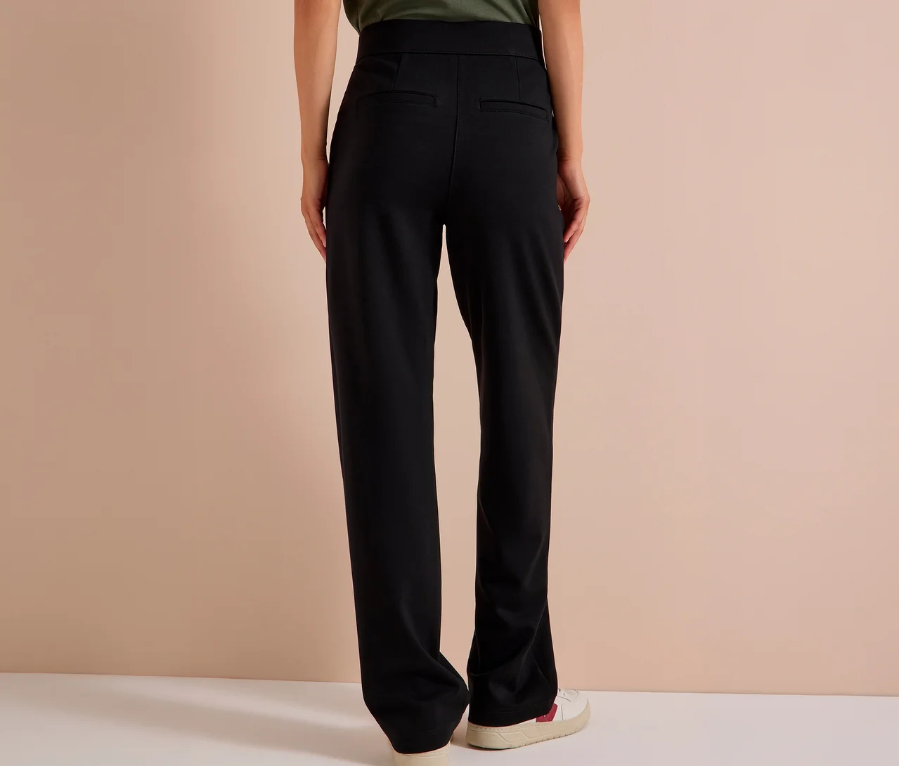 Personne de dos portant un pantalon en tissu CECIL noir et des baskets blanches.
