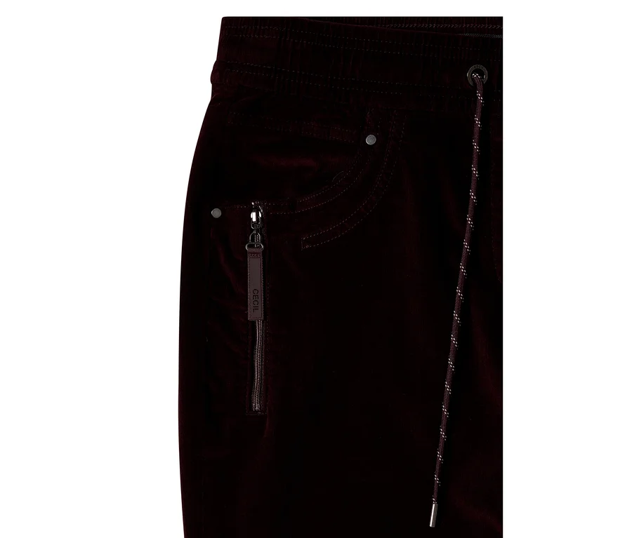 Gros plan d'un pantalon en velours côtelé CECIL rouge foncé avec une taille élastique, une poche zippée avec tirette « CECIL » et un cordon de serrage à embouts métalliques.