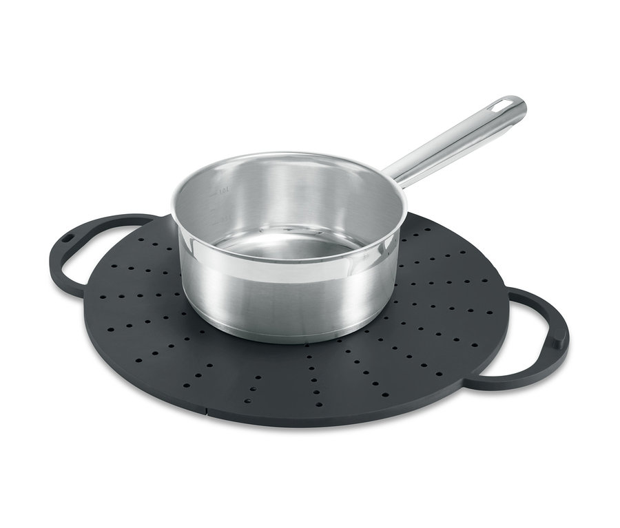 Une casserole en acier inoxydable est posée sur un ustensile de cuisson polyvalent noir avec des trous et des poignées.