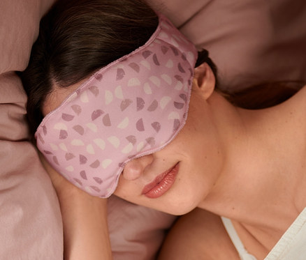 Femme dormant dans un lit avec un masque de nuit avec poids.
