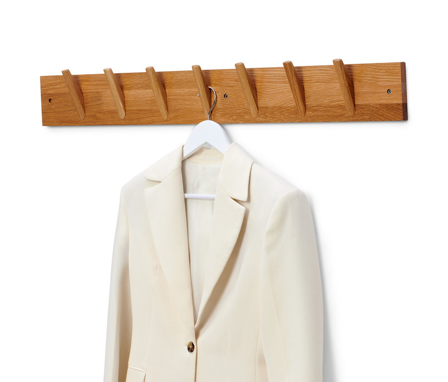 Un blazer beige est suspendu à un cintre blanc sur une garde-robe murale en bois massif.