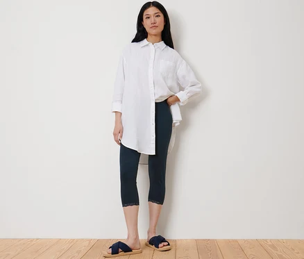 Une femme pose en legging 3/4 bleu foncé avec bordure en dentelle et une chemise blanche.