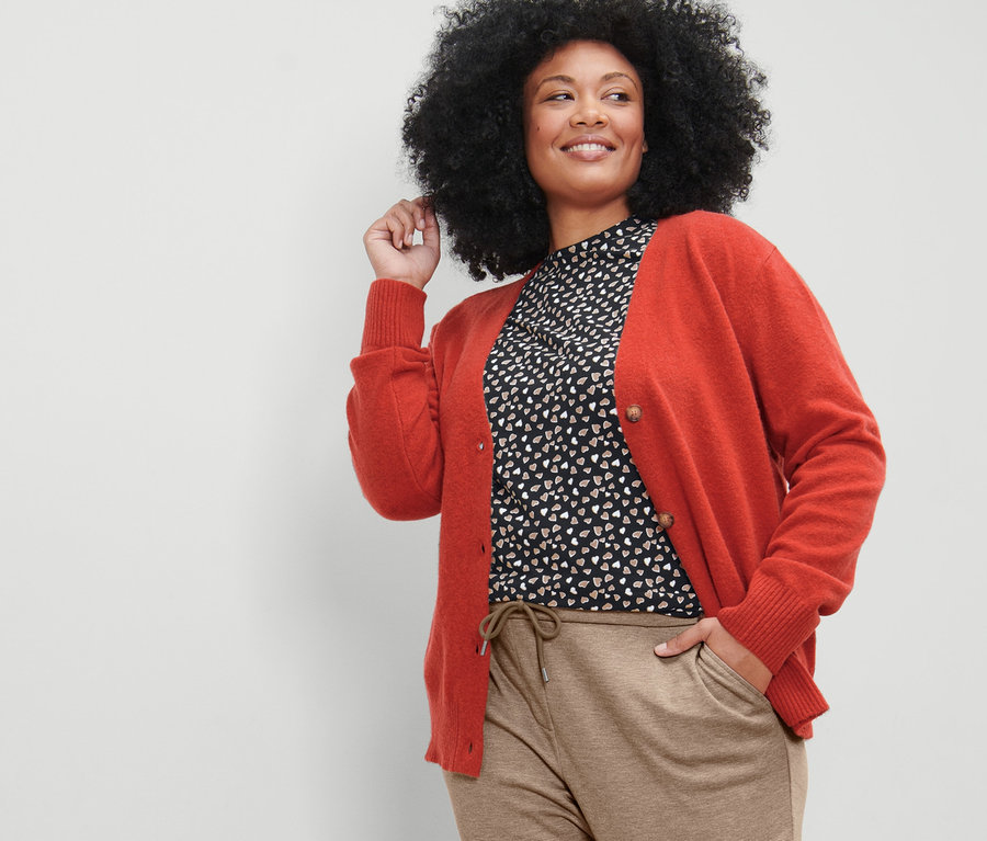Femme posant en cardigan à encolure en V, pantalon de jogging beige et t-shirt manches longues avec imprimé intégral.