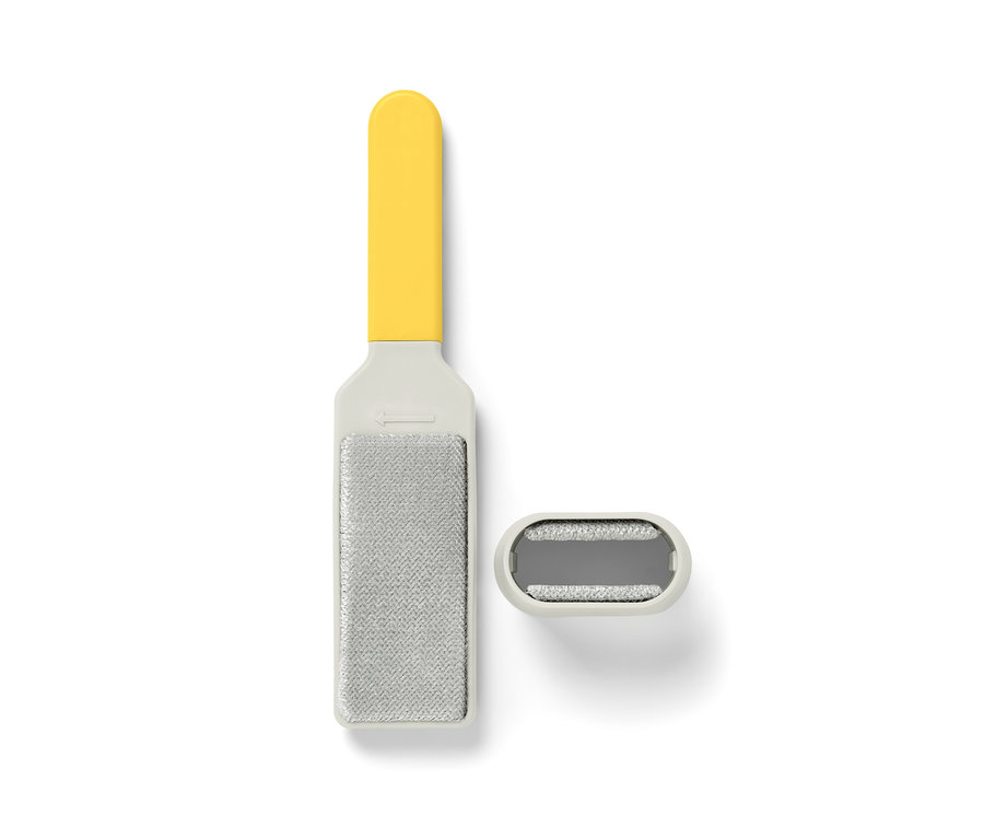 Une brosse à vêtements avec un manche jaune et un tampon de nettoyage reposent sur un fond blanc.