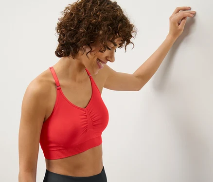 Une femme appuyée contre un mur porte une brassière de sport Seamless rouge.