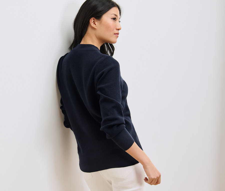 Une femme est appuyée contre le mur et porte un pull en maille fine bleu foncé.