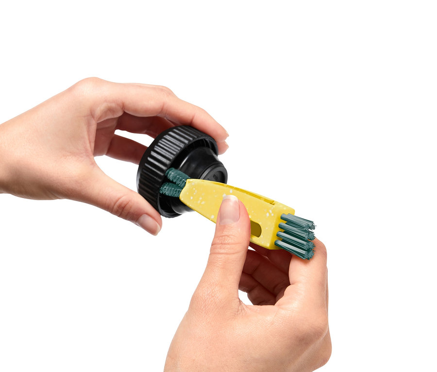 Une femme nettoie un bouchon noir avec une brosse multifonction 3 en 1 jaune.