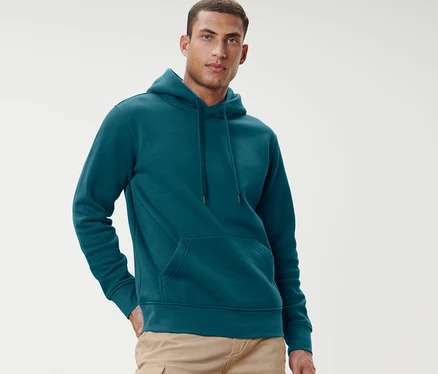 Un homme pose devant un fond clair, portant un sweat-shirt à capuche bleu pétrole.