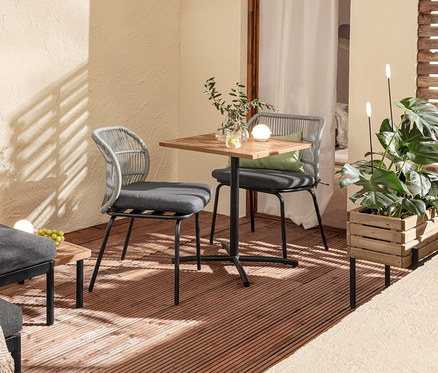 Balcon aménagé avec un ensemble lounge flexible « Elin », une table de balcon, des chaises avec tressage textile, 2 coussins d'extérieur, une caisse à plantes et 2 piquets lumineux solaires.