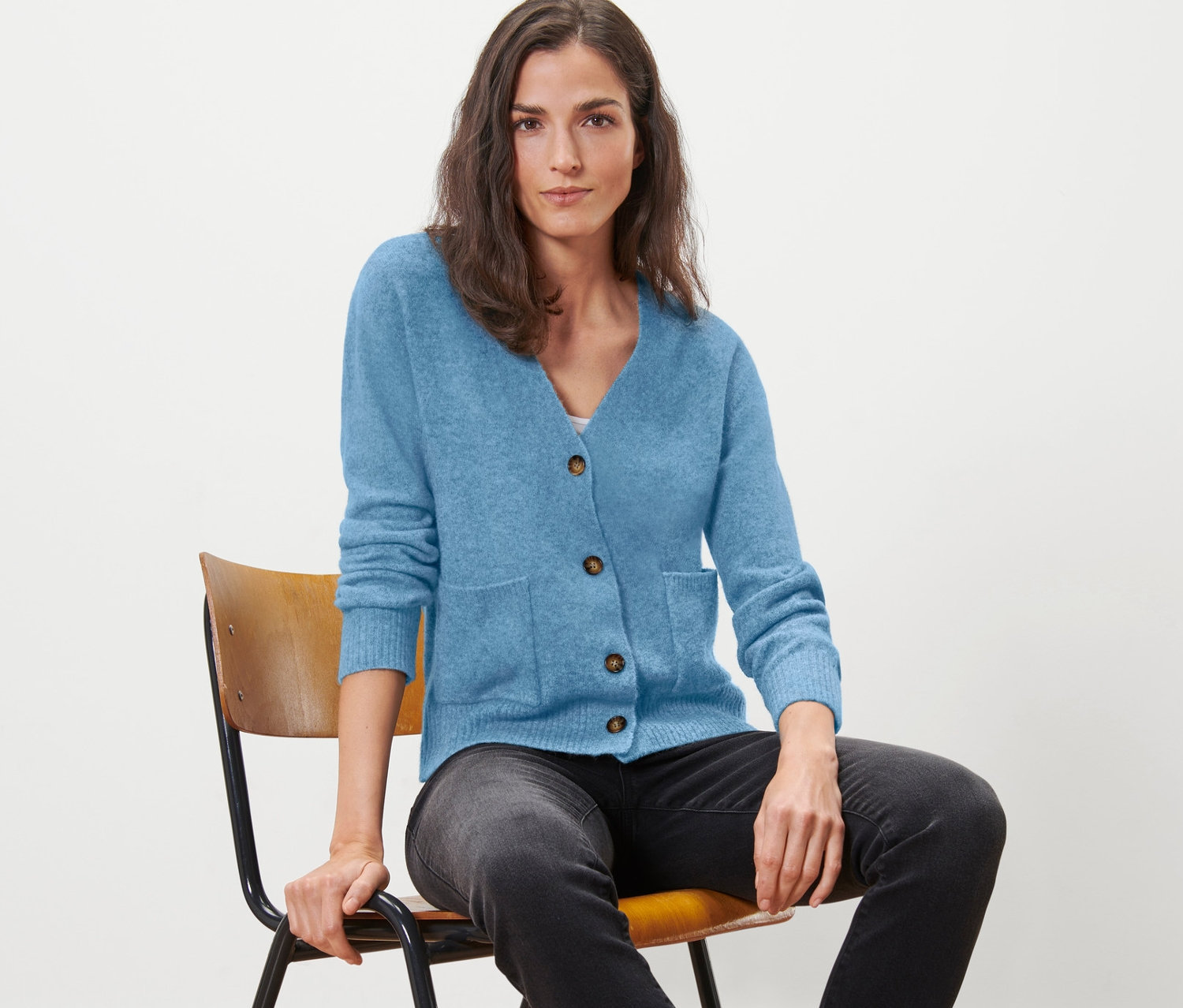 Une femme est assise sur une chaise et porte un cardigan en laine bleu clair.