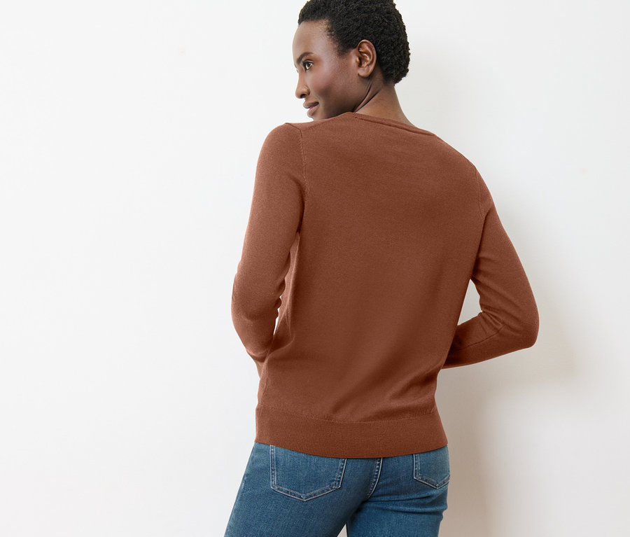 Une femme regarde par-dessus son épaule et porte un pull en maille fine mérinos couleur cognac.
