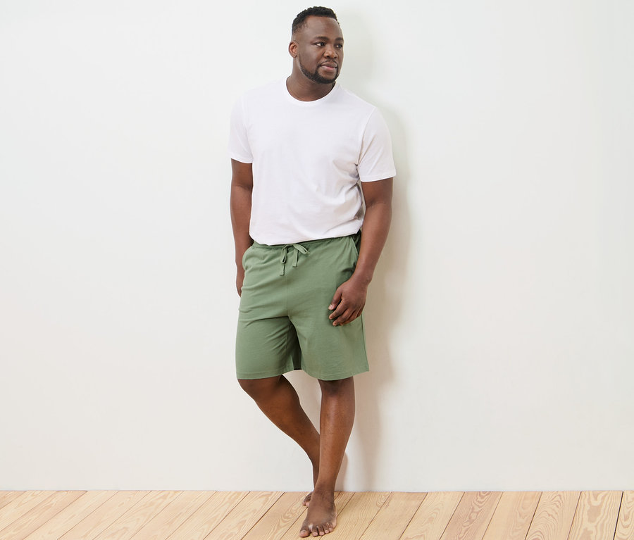 Un homme portant un t-shirt blanc et un short relax est debout contre un mur.