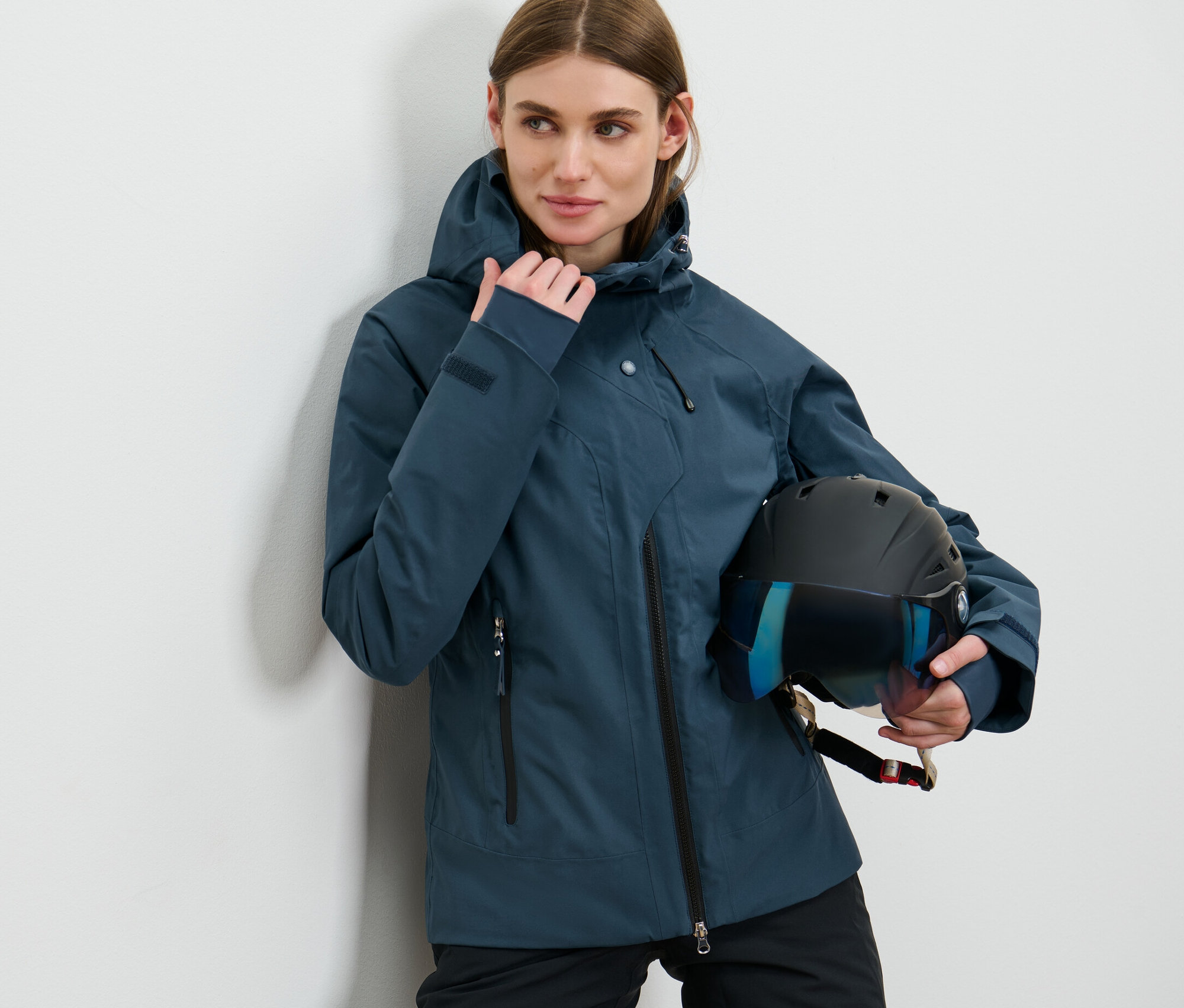 Femme posant en veste de ski bleu marine tenant un casque.