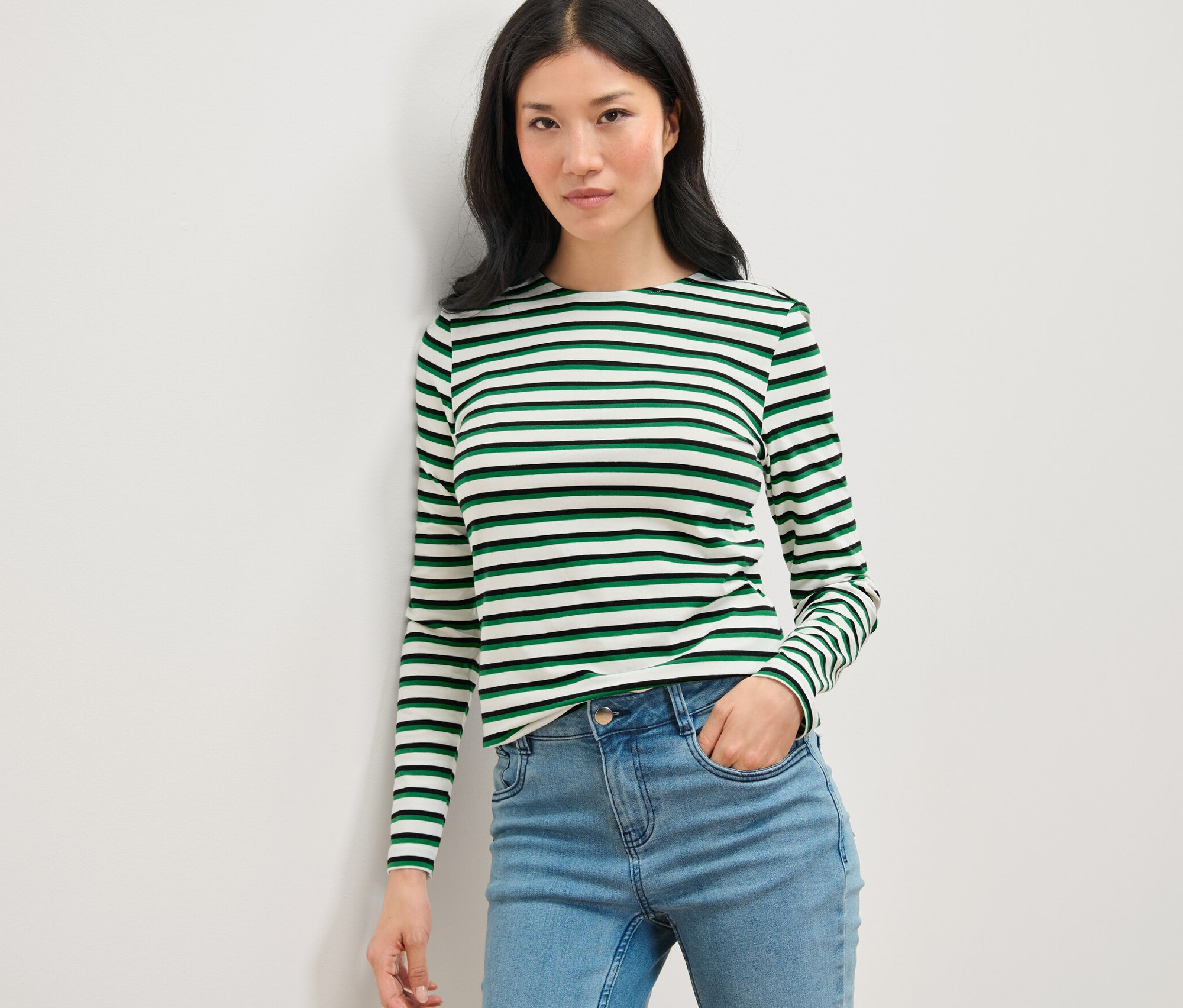 Femme posant dans un haut à manches longues rayé multicolore et un jean.