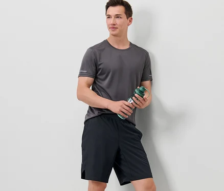 Un homme tient une bouteille d'eau et porte un short de sport.
