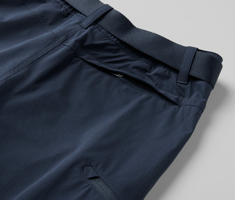 Détail d'un pantalon technique 2 en 1 bleu avec poches zippées et ceinture.