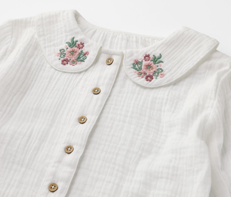 Gros plan d'une blouse en mousseline pour enfant avec broderie florale sur le col et boutons.