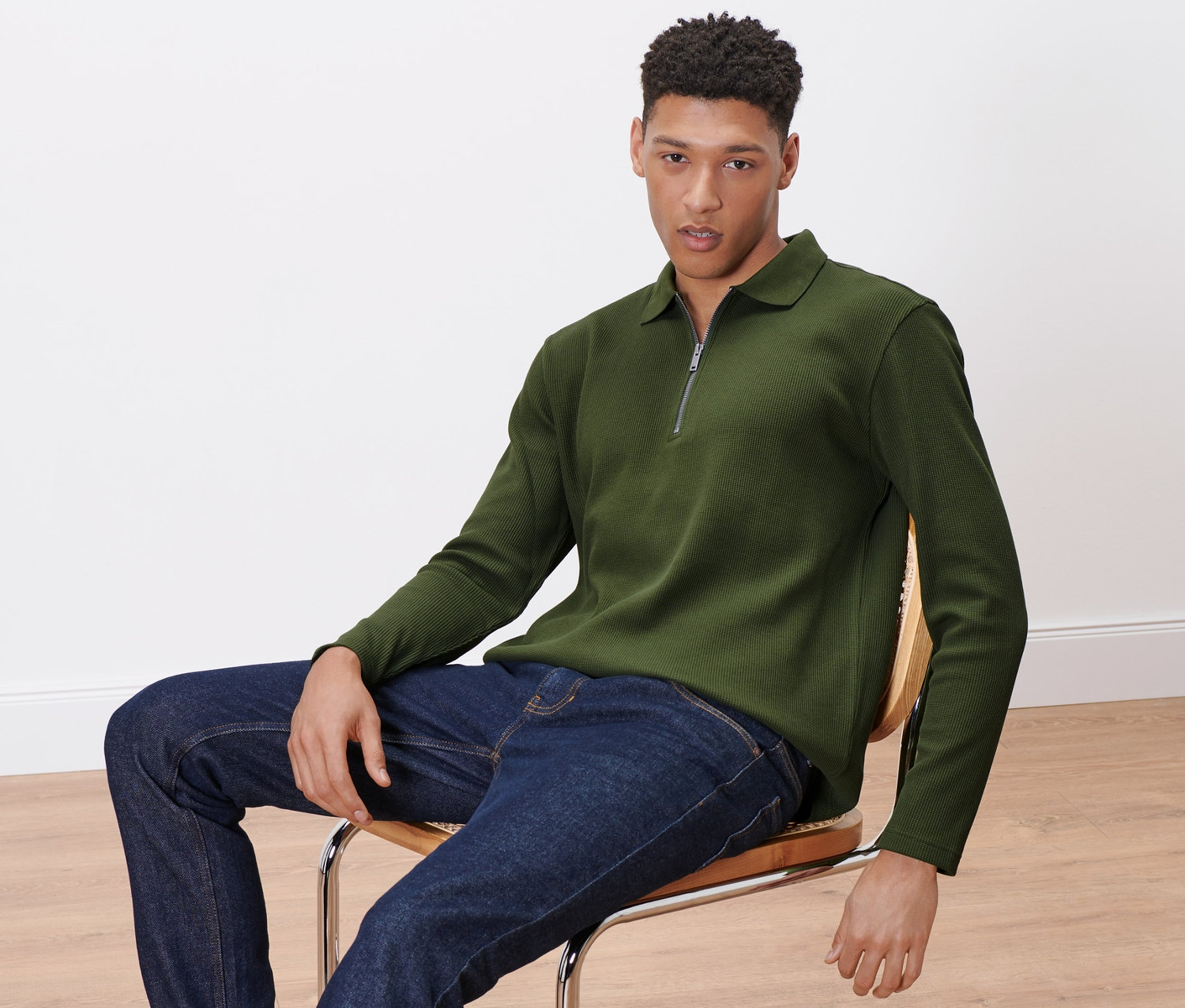 Un homme est assis sur une chaise et porte un polo à manches longues.