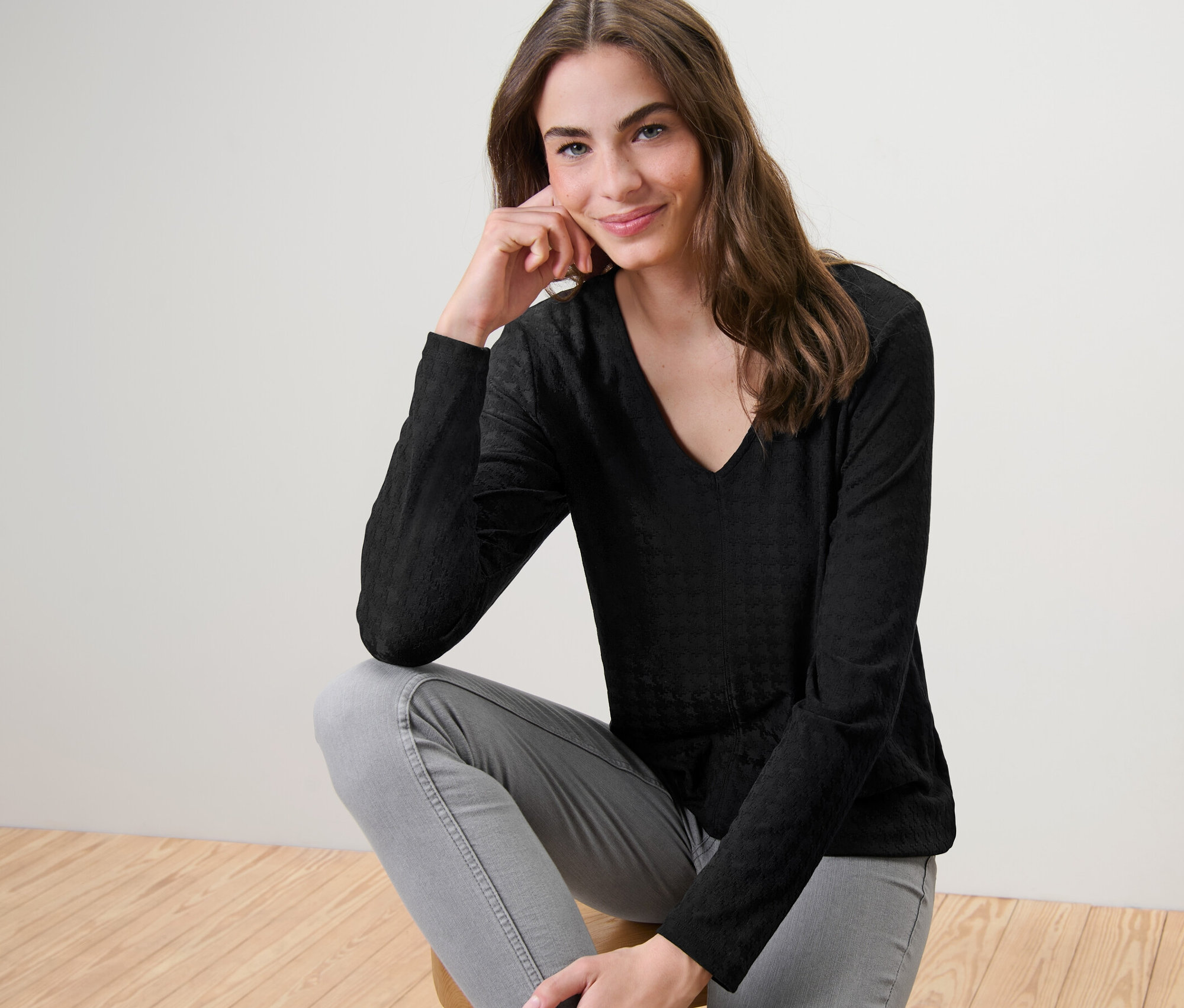 Une femme est assise sur un tabouret et porte un t-shirt à manches longues structuré noir.