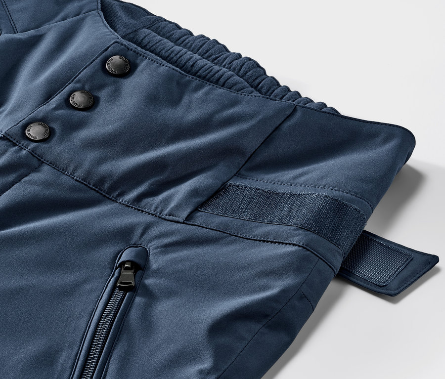 Gros plan sur un pantalon de ski taille haute bleu. Détails des boutons, de la fermeture éclair et du velcro.