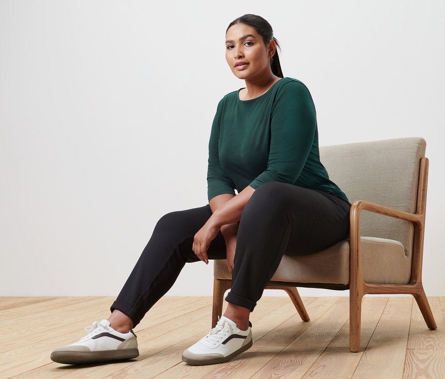 Femme assise dans un fauteuil portant un t-shirt manches 3/4 vert foncé.